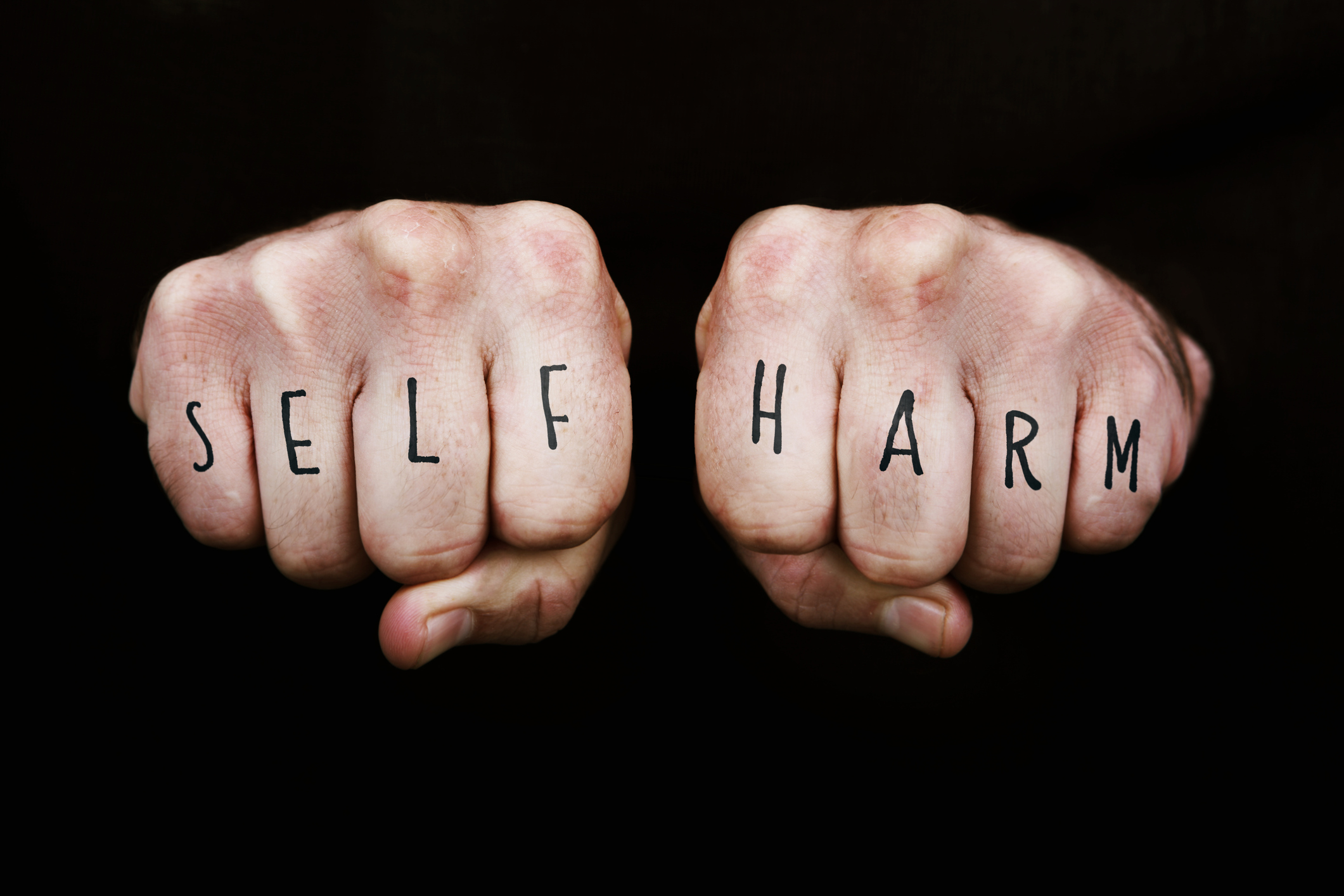 Self Harm written across the knuckles of two clenched fists